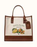 Front of the canvas tote on cream: SANTA PALMA over ORGULLOS DE NUESTRA TIERRA, with guineos, a mango and a halved lechosa printed beneath, tobacco leather at the base, the binding and the handles.