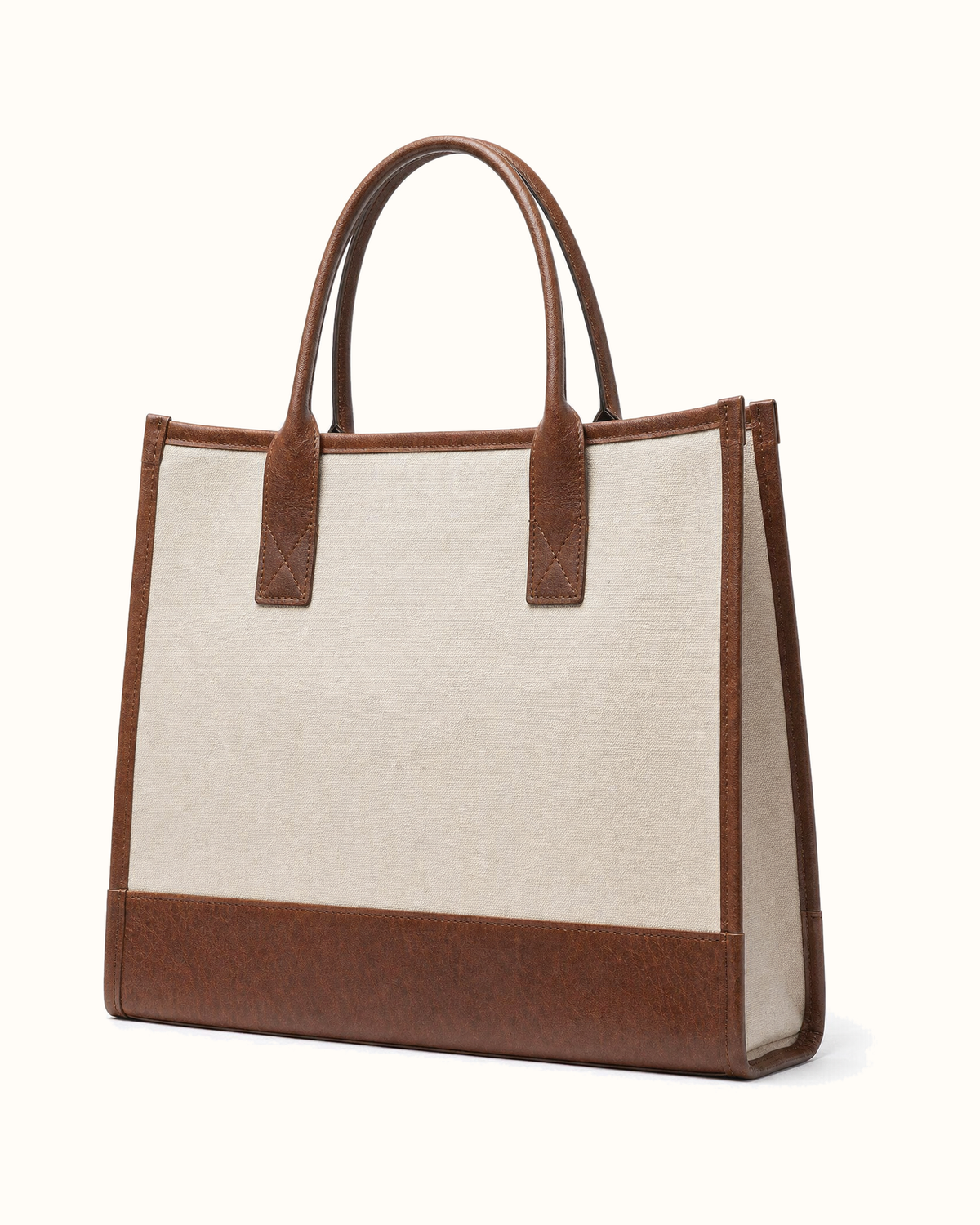 The same tote from behind, turned three-quarter: plain canvas, no print, leather base and corner binding, both rolled handles standing.