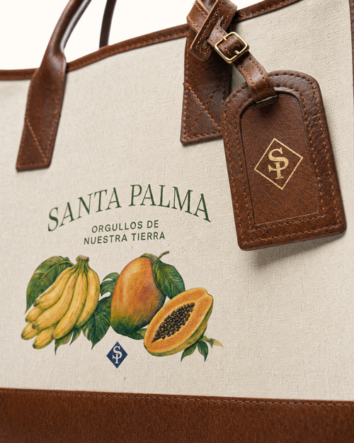 Close on the printed panel: SANTA PALMA in green above guineos, a mango and a halved lechosa, the blue SP diamond between them, and the gold SP diamond stamped on the leather tag alongside.