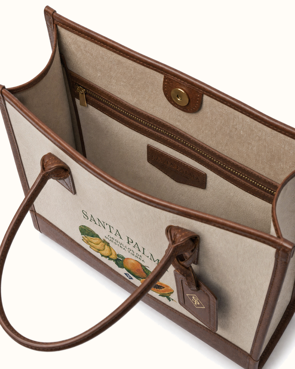 Looking down into the open tote: pale canvas lining, a leather-bound zip pocket with its brass pull, the SANTA PALMA patch stamped inside the front wall, the turn-lock tab above it, and the leather luggage tag hanging outside.