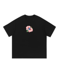 Black boxy tee, front: pink Rosa de Bayahíbe blooms and green leaves clustered around a small blue SP diamond.